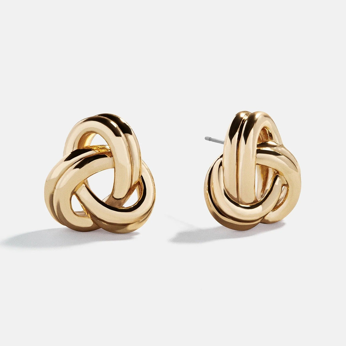 Lavisa glossy gold knot statement earrings resting on a neutral surface